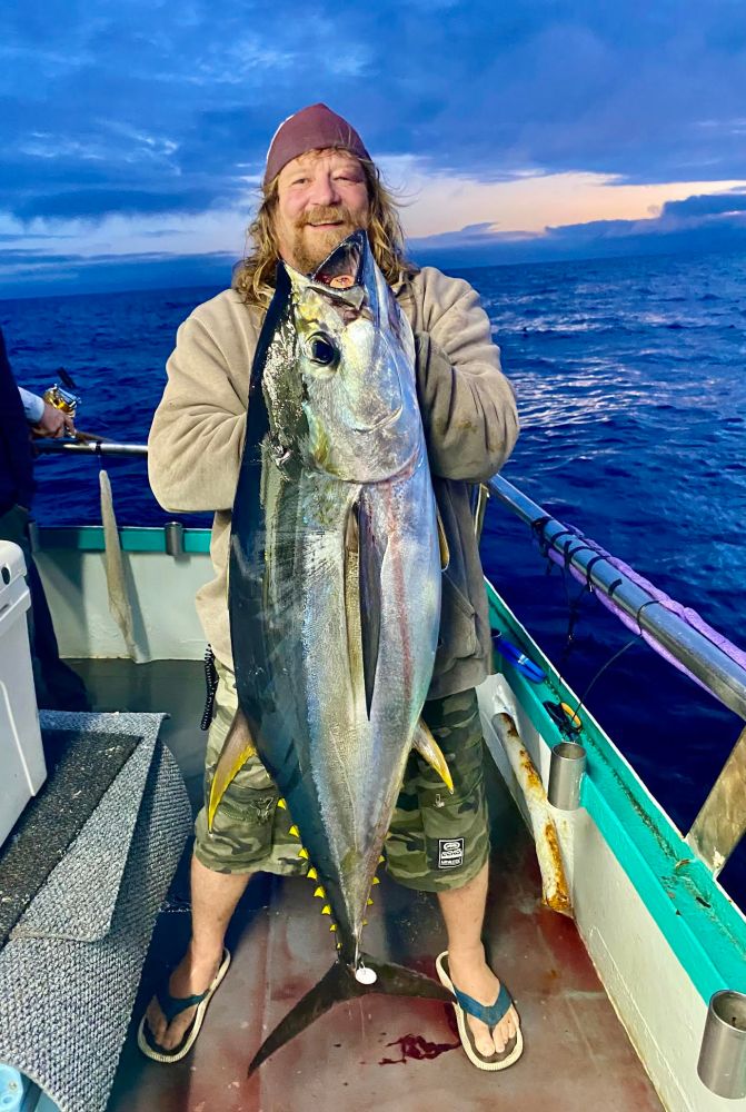 Person on a boat holding a large fish against a blue evening sky.