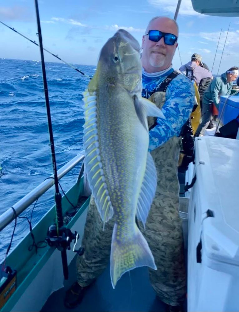Person on a boat holding a large fish with fishing rods in the background.