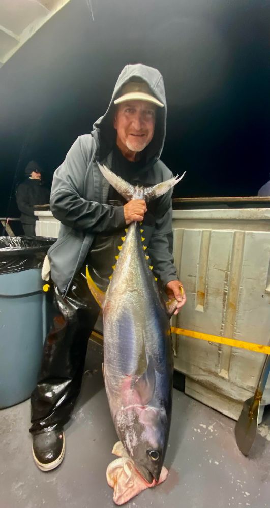 Person holding a large fish on a boat deck at night.