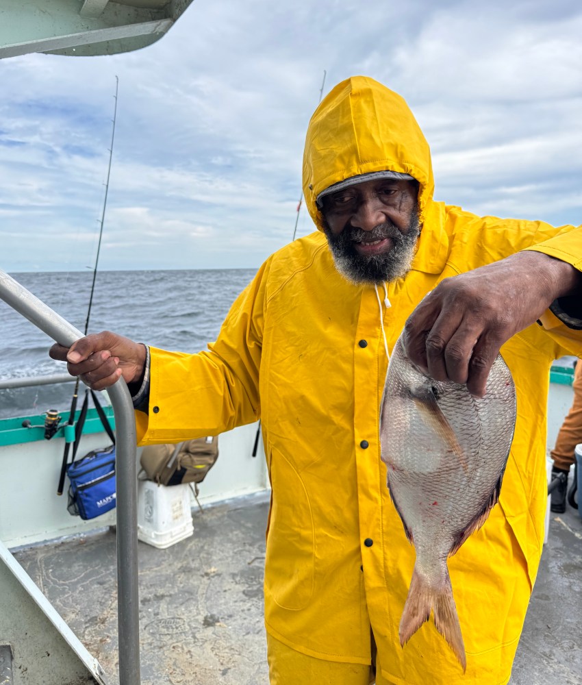 Person in yellow raincoat holding a fish on a boat with ocean in the background.