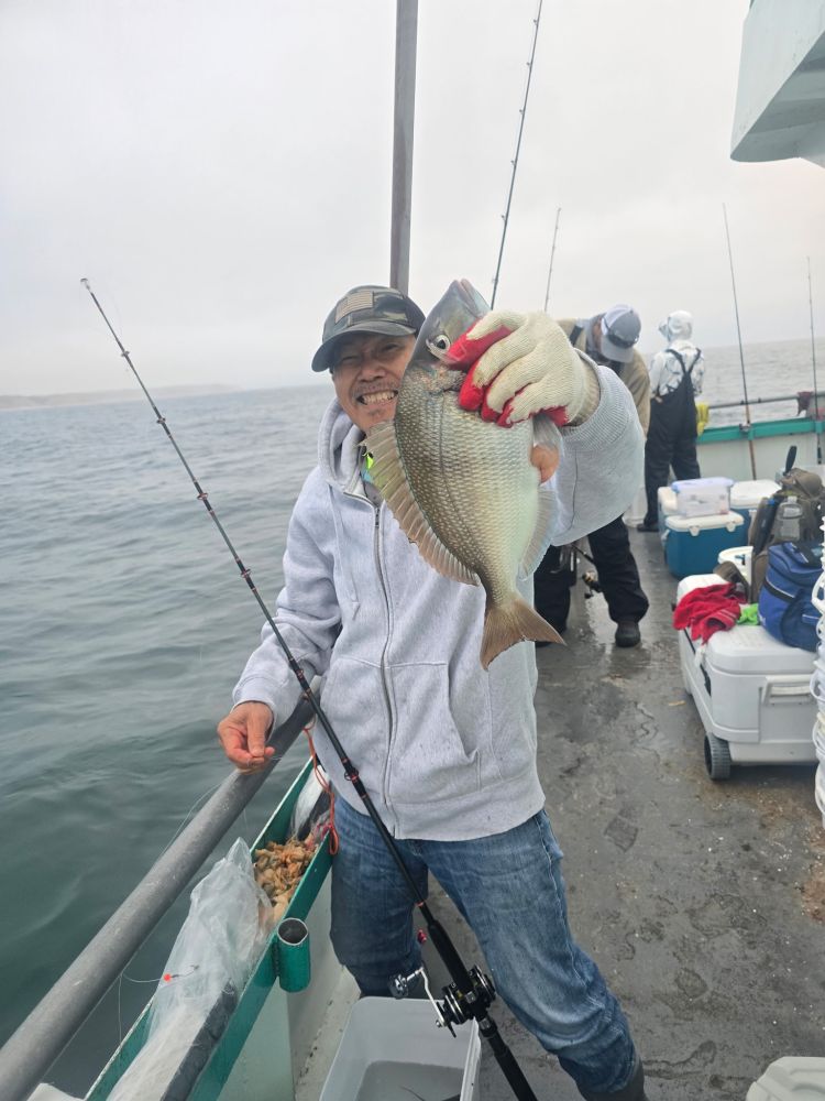 Person smiling, holding a fish on a boat with fishing rods and ocean in background.