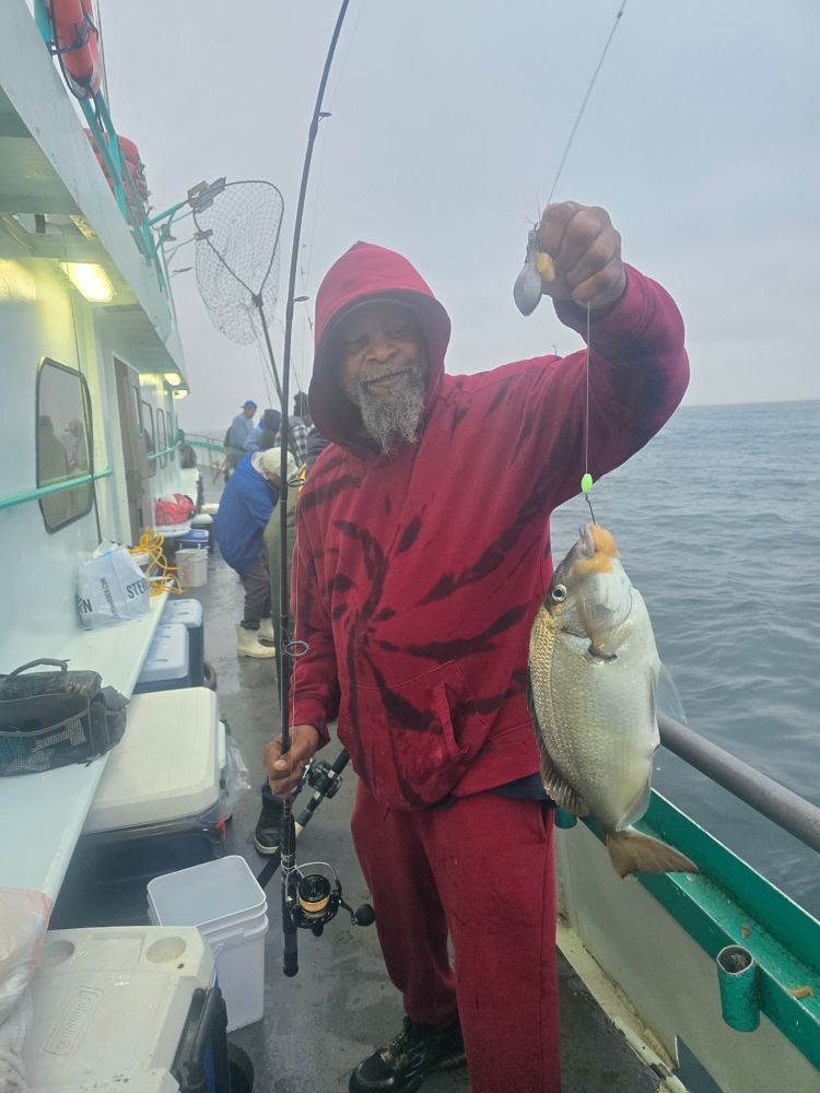 Person in red hoodie holding a fish on a boat with fishing gear.