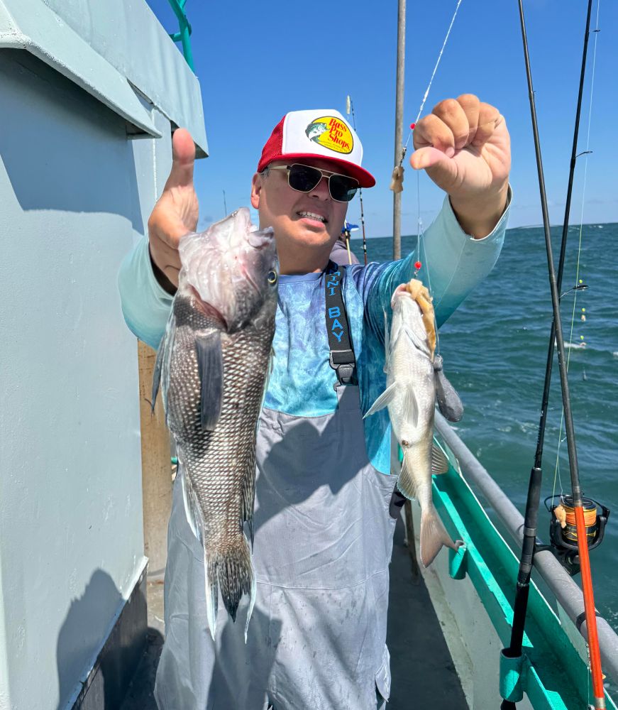 Person on boat holding two fish, with a fishing rod in the background.