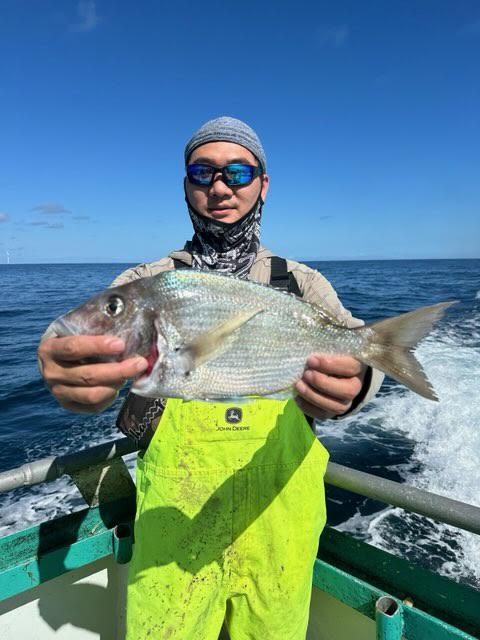 Person in bright yellow overalls holding a large fish on a boat with ocean in the background.