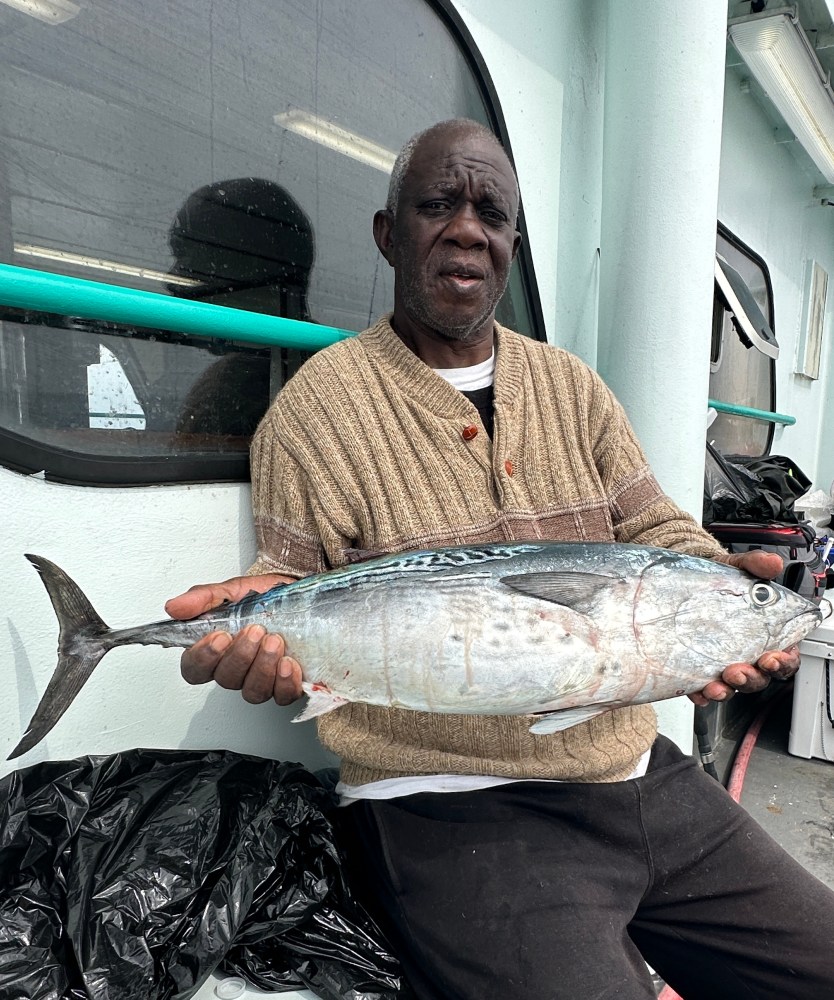 Person holding a large fish on a boat, with a window and equipment in the background.