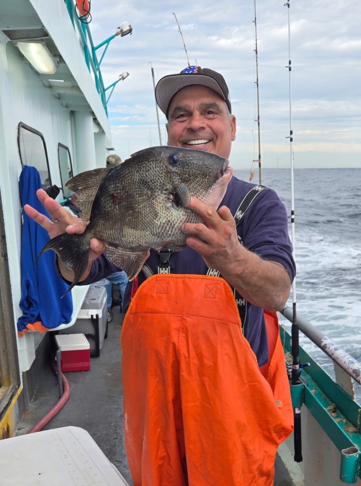 Person on a boat holding a large fish, wearing orange overalls.