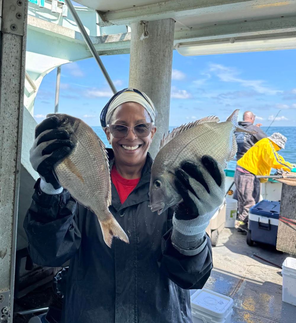 Person on a boat holding two fish, smiling at the camera.