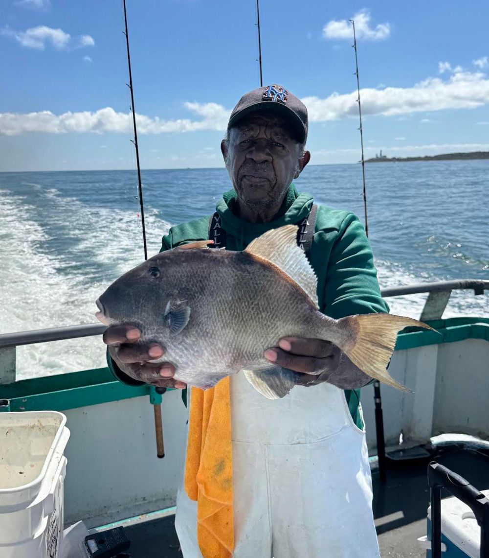 Person on a boat holding a large fish with the ocean in the background.