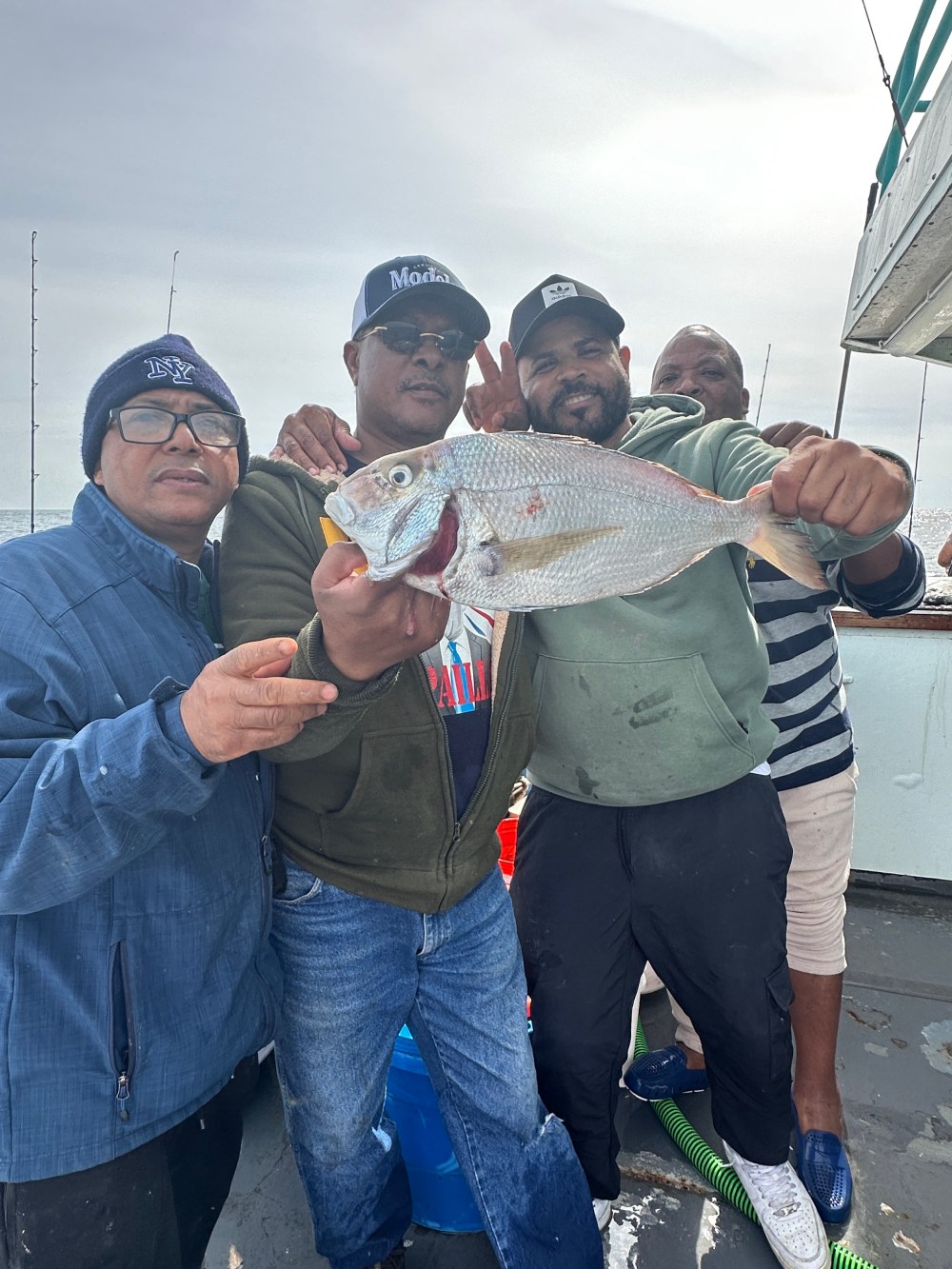 Four men on a boat holding a large fish, smiling at the camera.