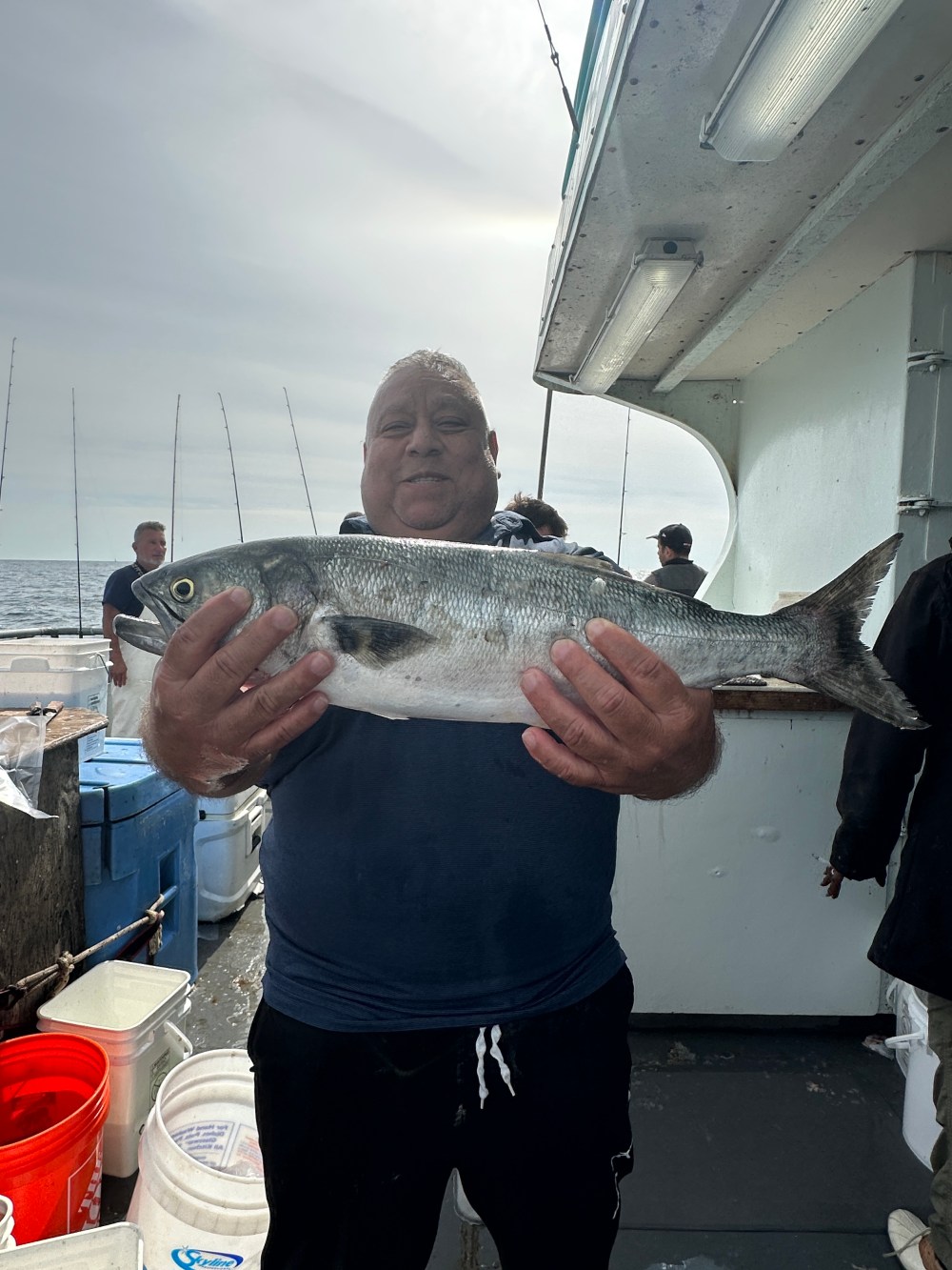 Person holding a large fish on a boat with fishing rods and buckets visible.