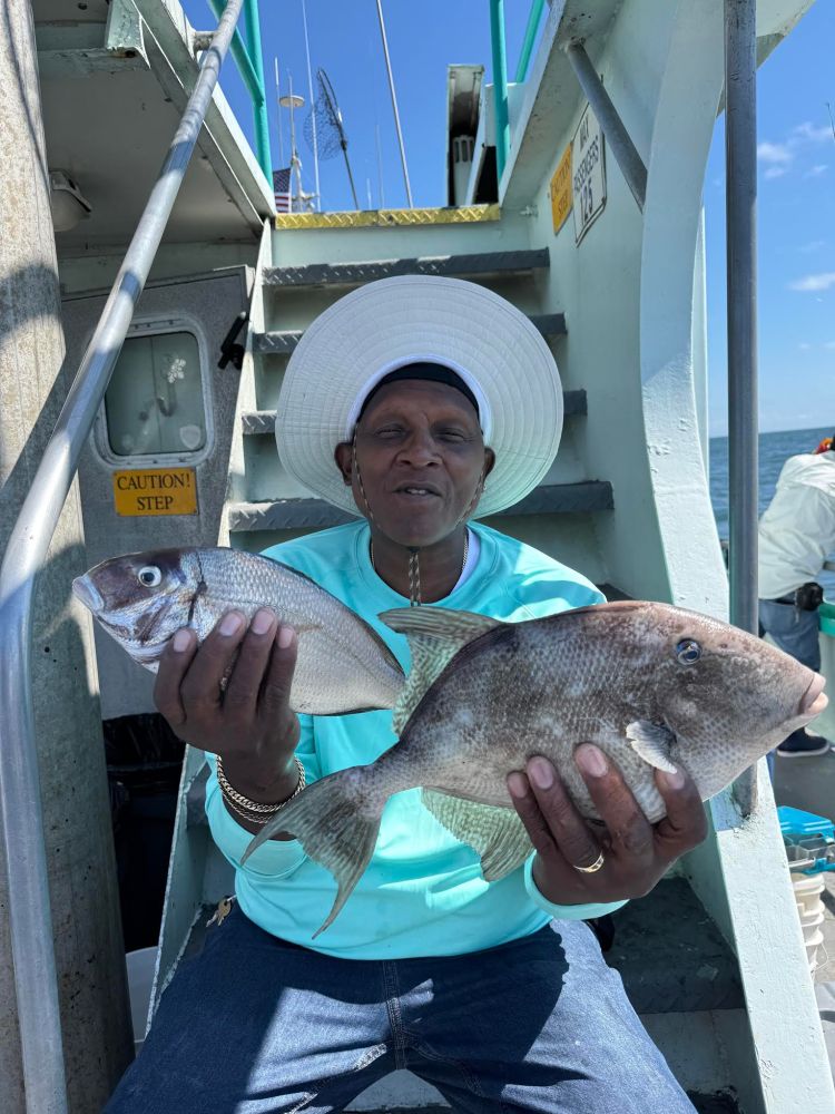 Person in a hat holding two fish while sitting on a boat's stairs.