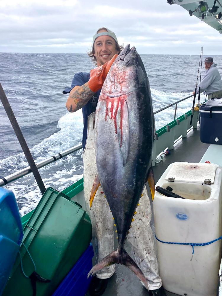 Person holding a large fish on a boat at sea with another person in the background.
