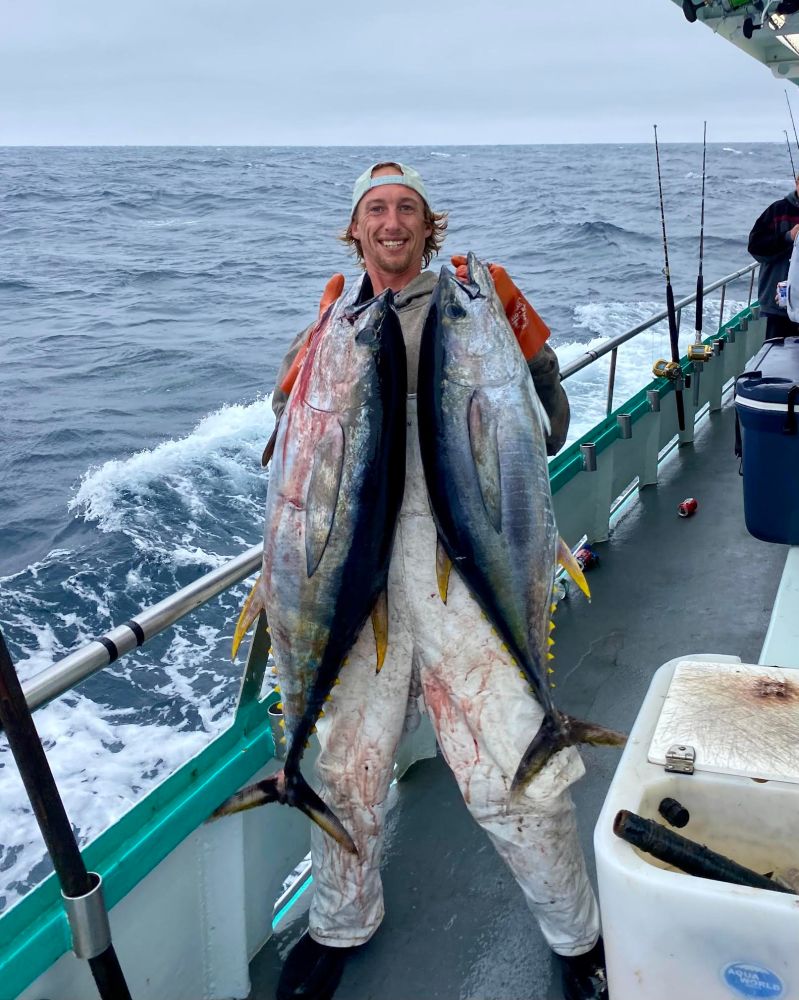 Person holding two large fish on a boat with ocean in the background.