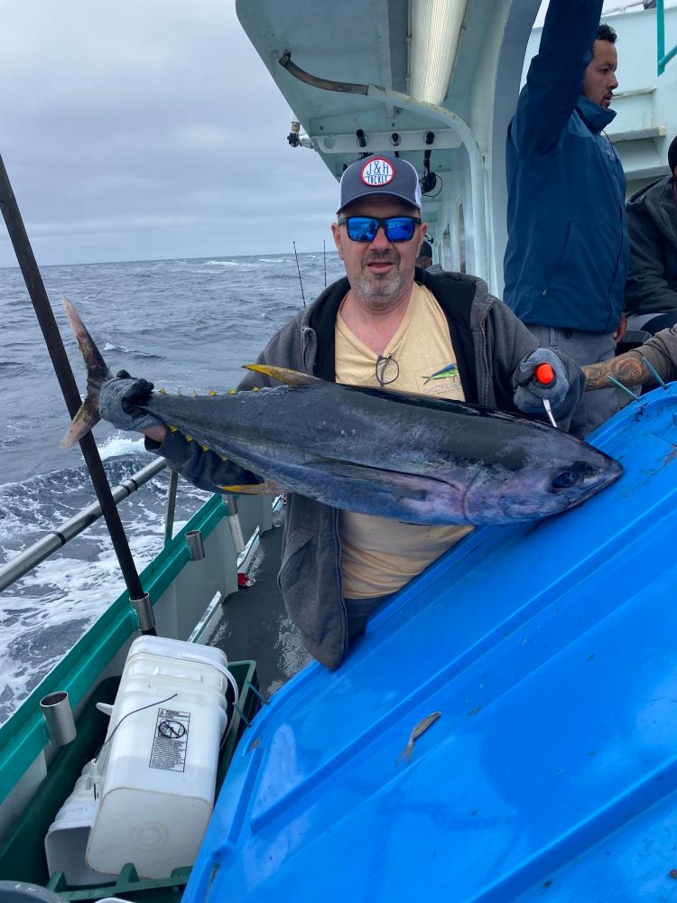 Man on boat holding large fish with ocean in the background.