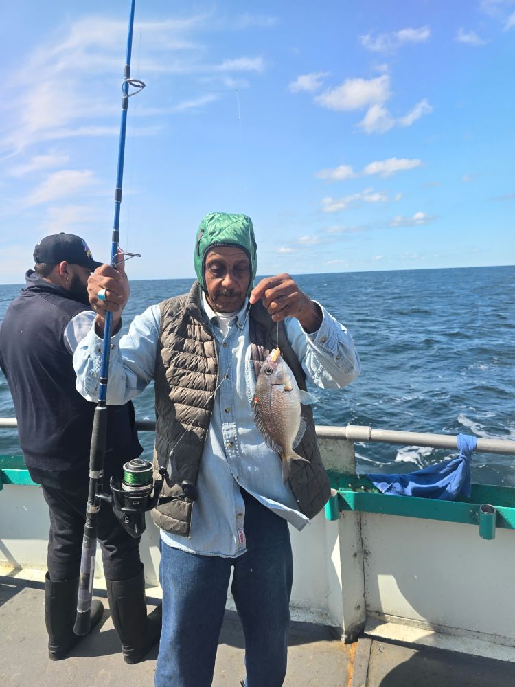 Person holding a fish and fishing rod on a boat with ocean backdrop.