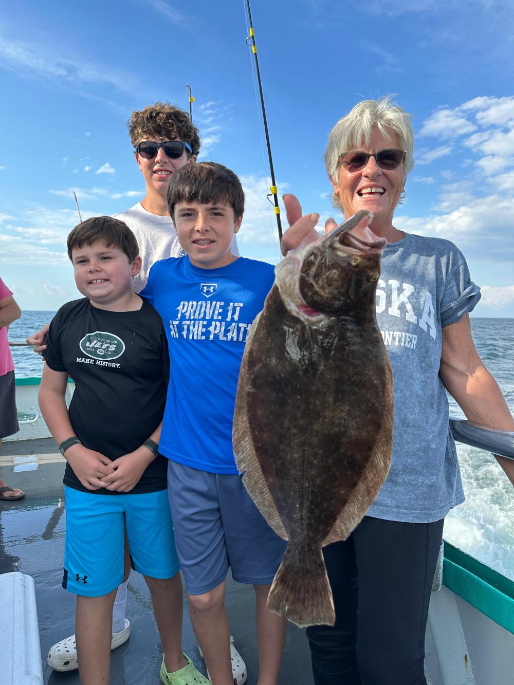 Group of people on a boat smiling, with one person holding a large fish.