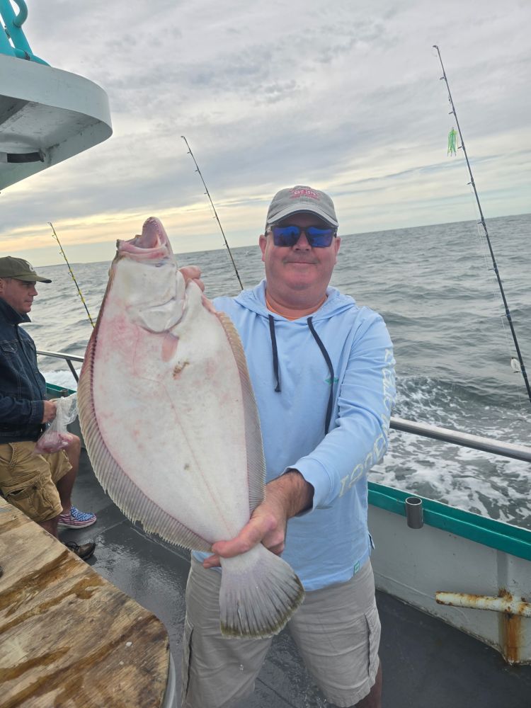 Man on boat holding a large fish with the ocean in the background.