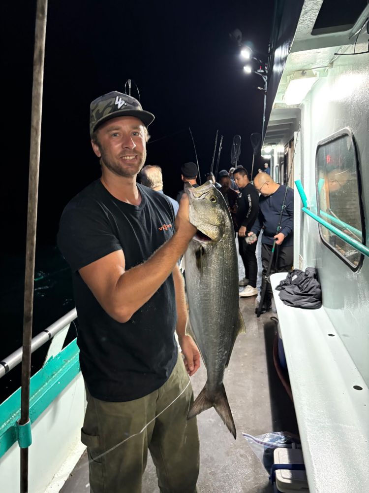 Man holding a large fish on a boat at night with others in the background.