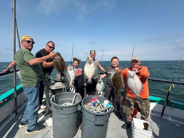 Six people on a boat proudly hold up their fish catches near the ocean.