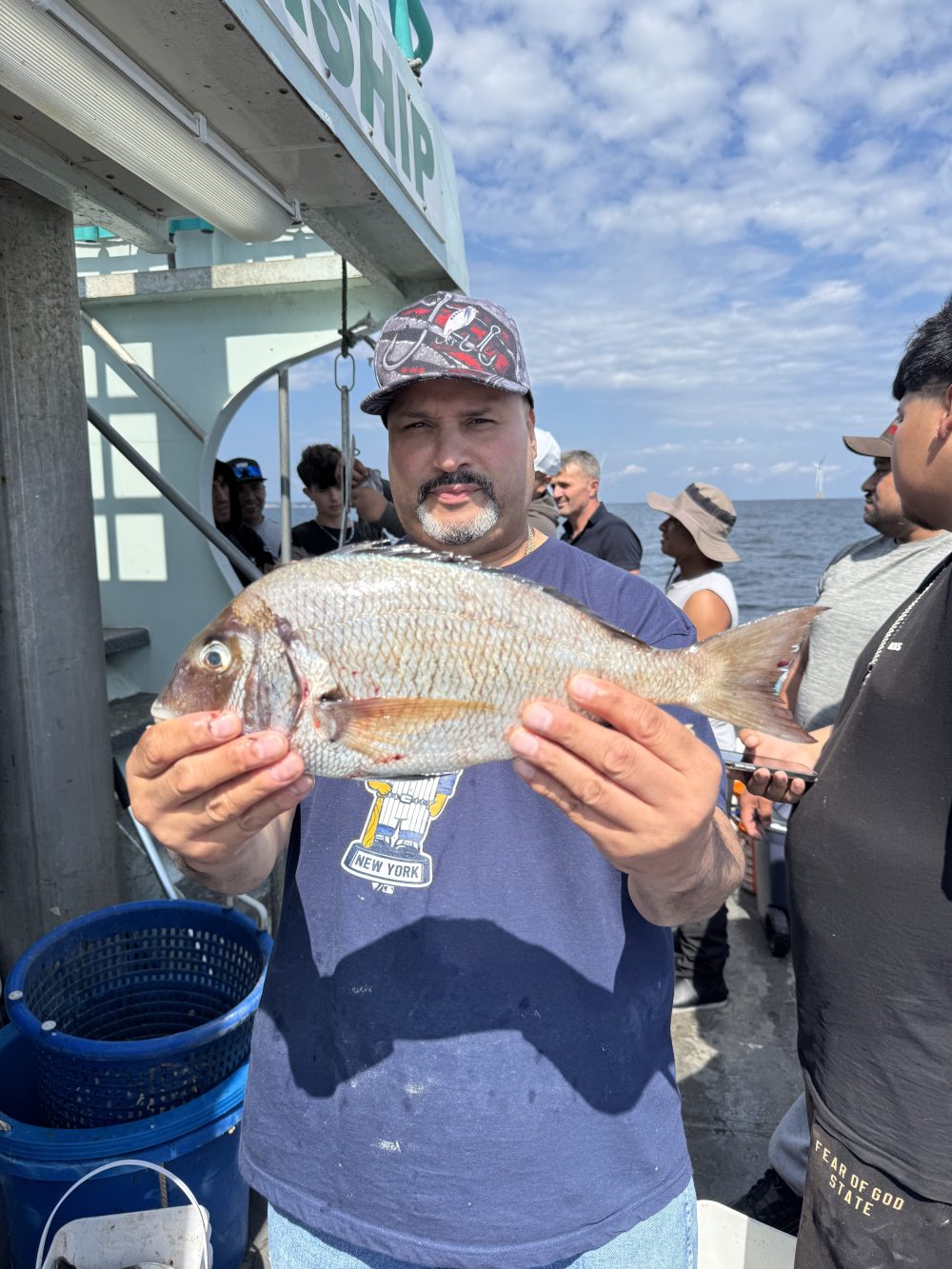 Man holding a fish on a boat with people and ocean in the background.