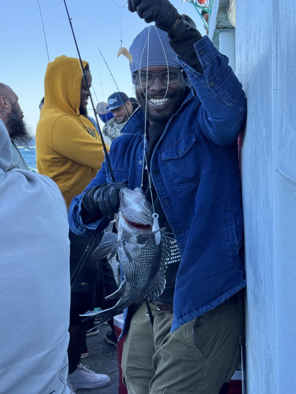 Person smiling and holding a caught fish on a boat with others around.