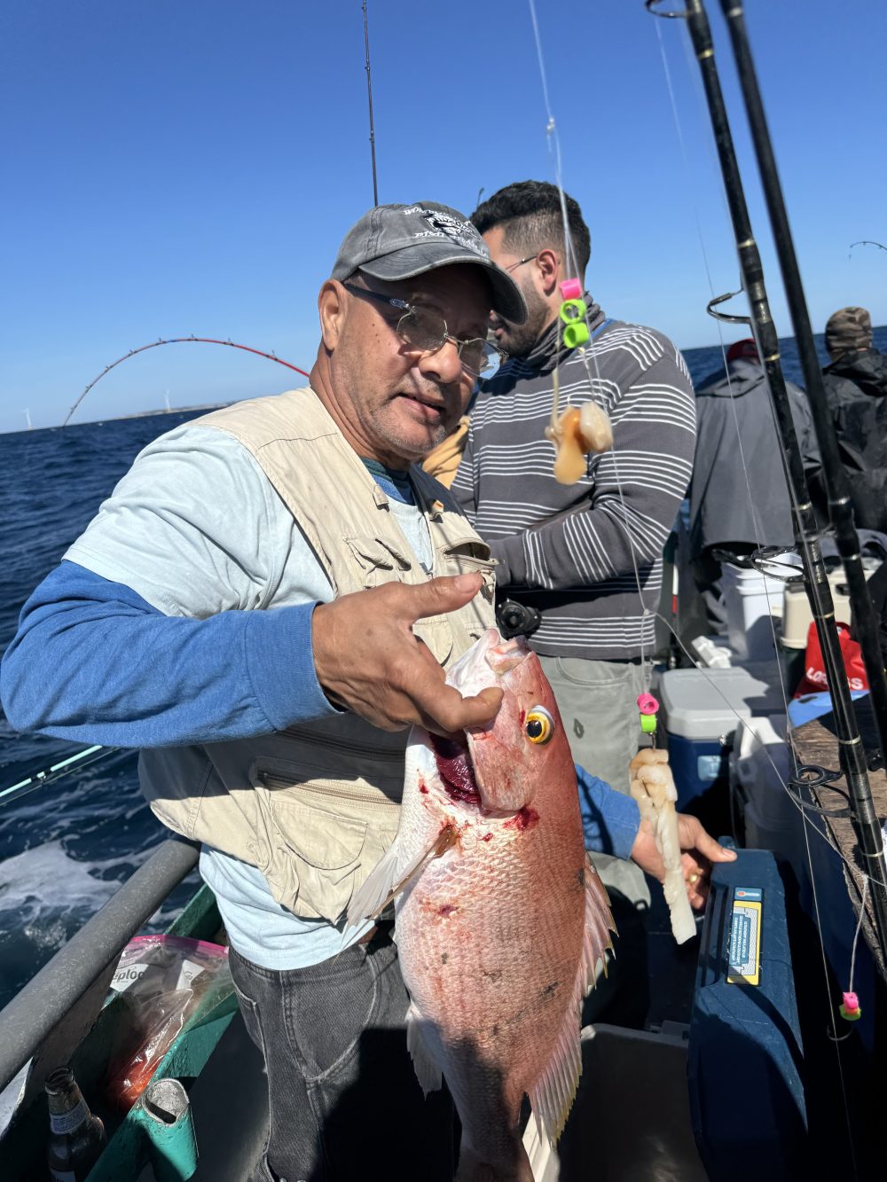 Man holding a large fish on a boat with fishing gear on a sunny day.