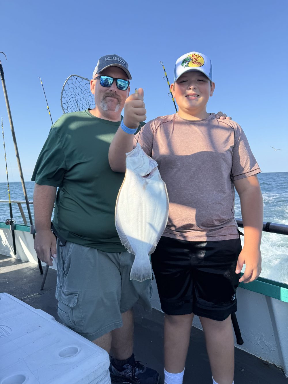 Two people on a boat holding a flat fish with fishing rods in the background.