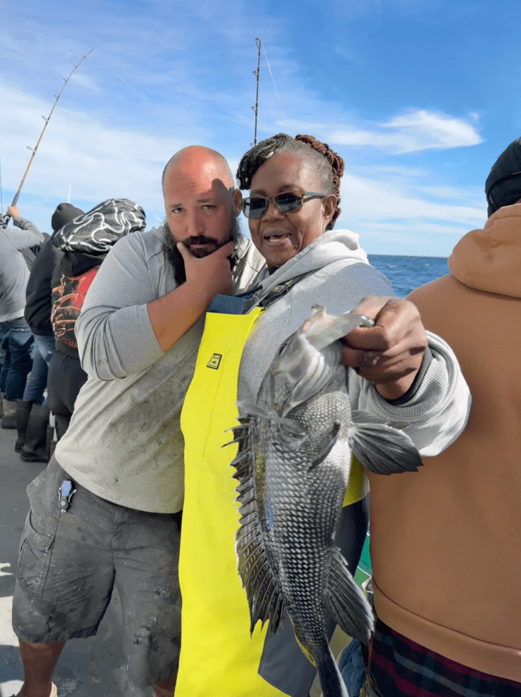 Two people on a boat holding a fish; one is wearing a yellow bib.