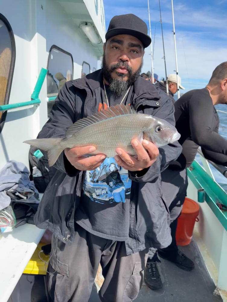 Man holding a fish on a boat with others in the background.