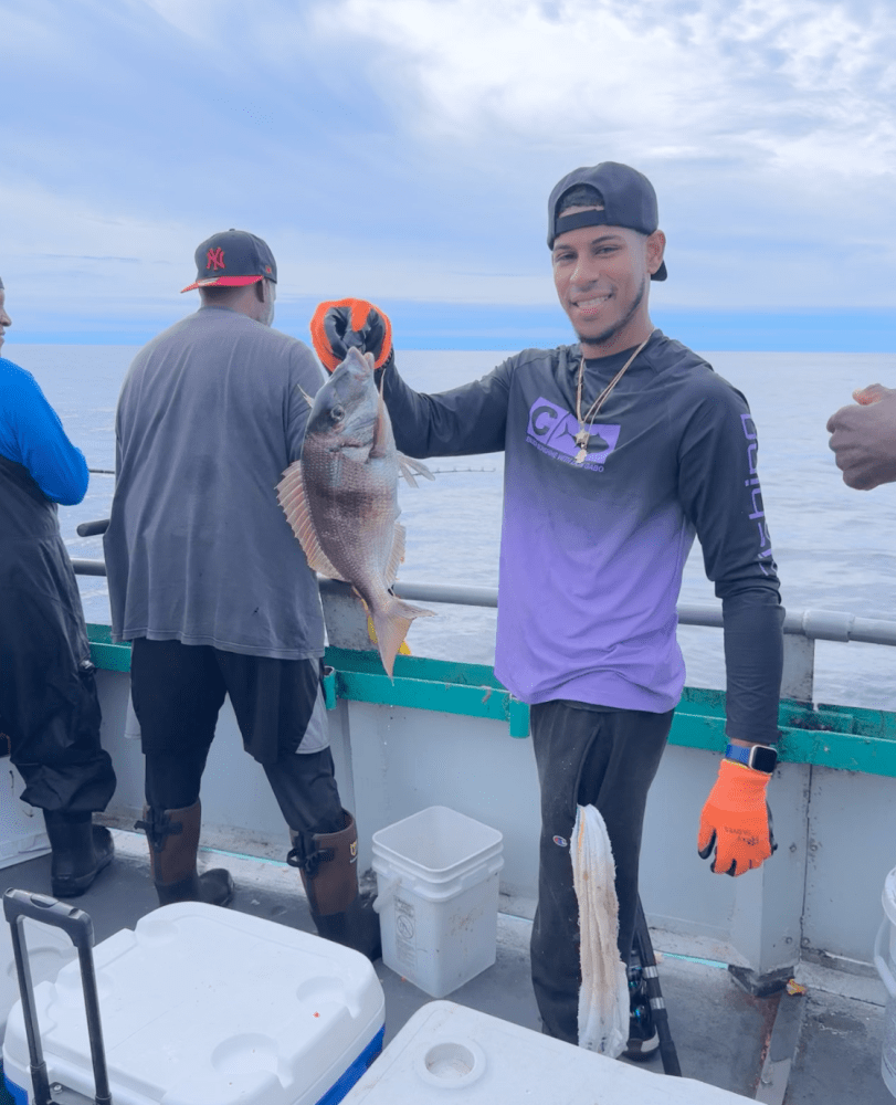 Man in purple shirt holding a fish on a boat with two other people visible.