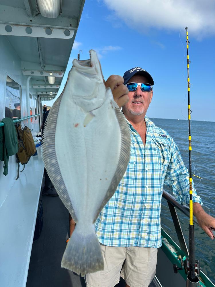 Person holding up a large flounder on a fishing boat.