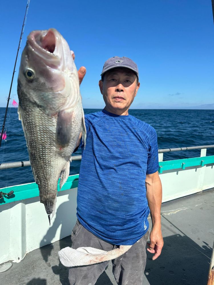 Person in blue shirt holding a large fish on a boat with ocean background.