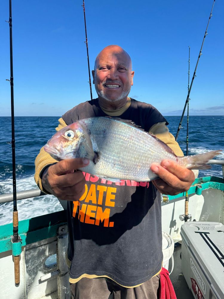 Man on boat holding fish, smiling; fishing rods and ocean in background.