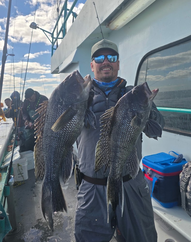 Person on boat holding two large fish, wearing sunglasses and cap.