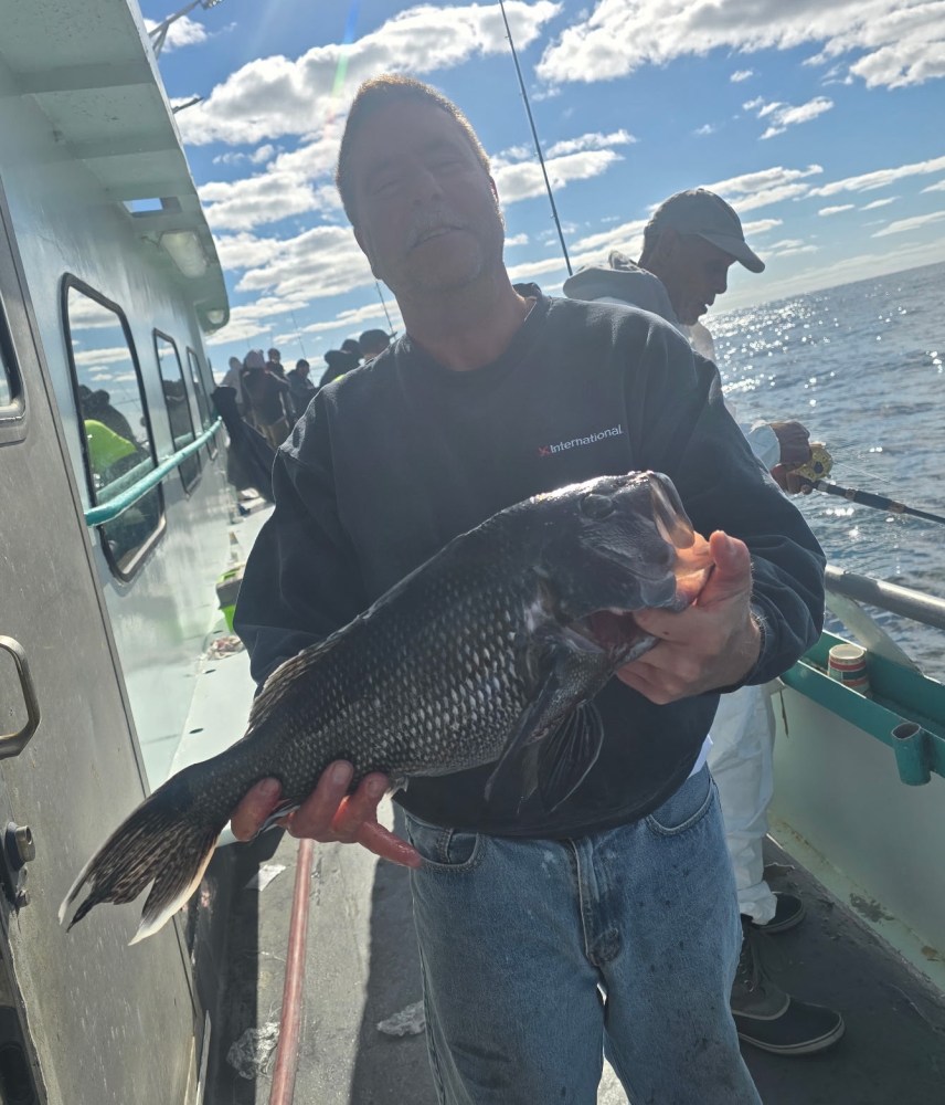 Person holding a large fish on a boat with others fishing in the background.