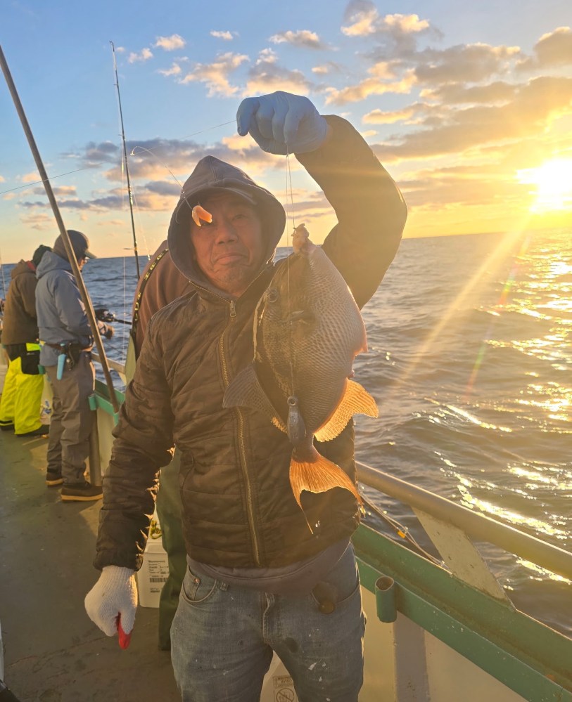 Person on a boat holding a fish with the sun setting over the ocean.