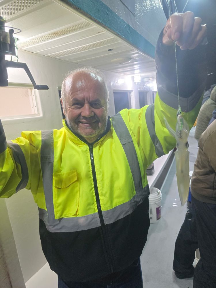 Man in hi-vis jacket holding a squid on a boat at night.