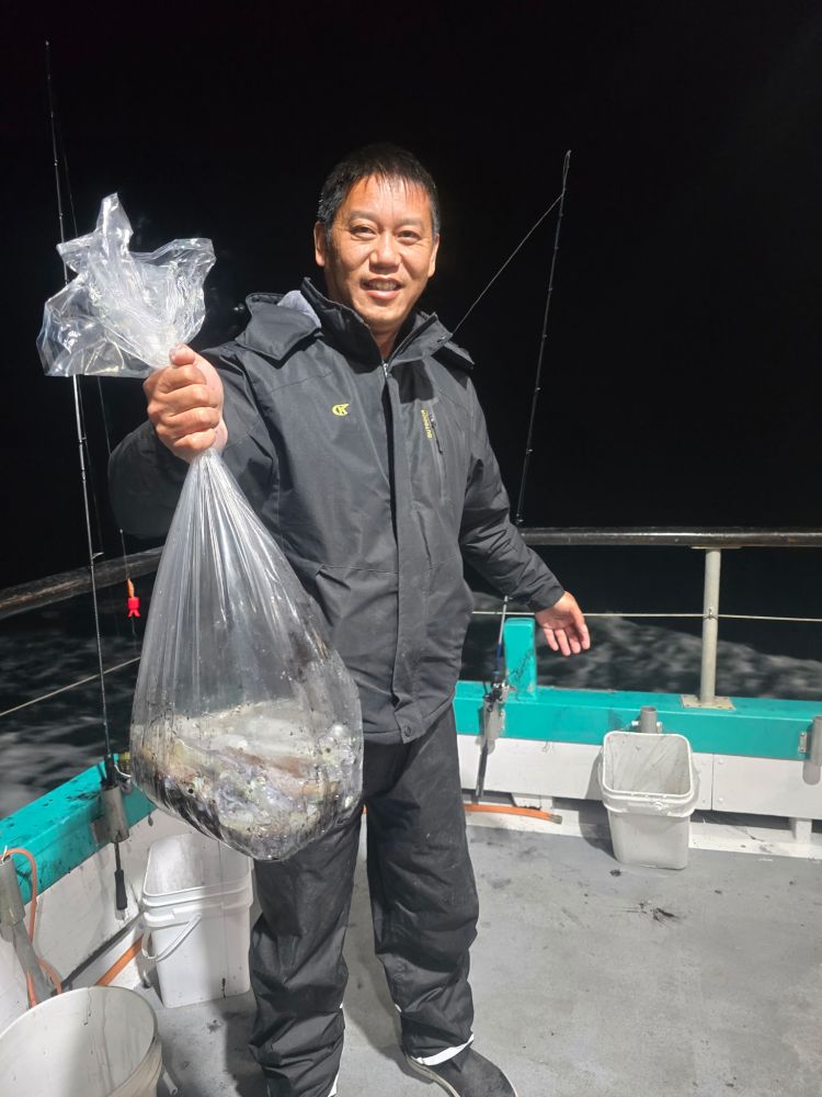 Person in a dark jacket holding a bag of fish on a boat at night.
