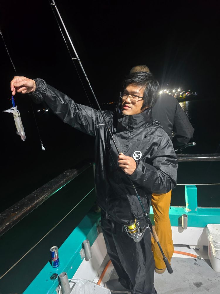 Person on a boat at night holding a fishing rod with a small squid.
