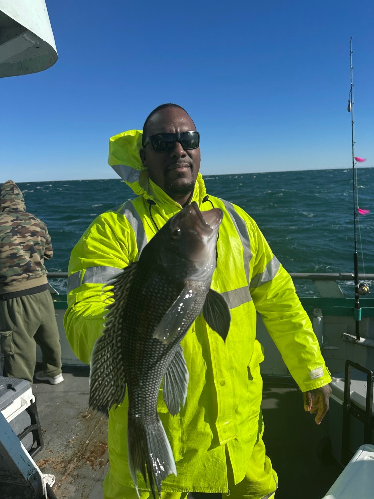 Person in bright jacket holding a fish on a boat, with ocean and sky in the background.