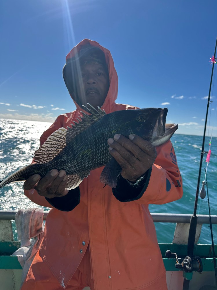 Person in orange raincoat holding a fish on a boat under a clear blue sky.