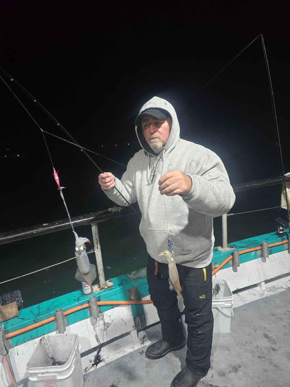 Person on a boat at night holding fishing lines with two caught squids.