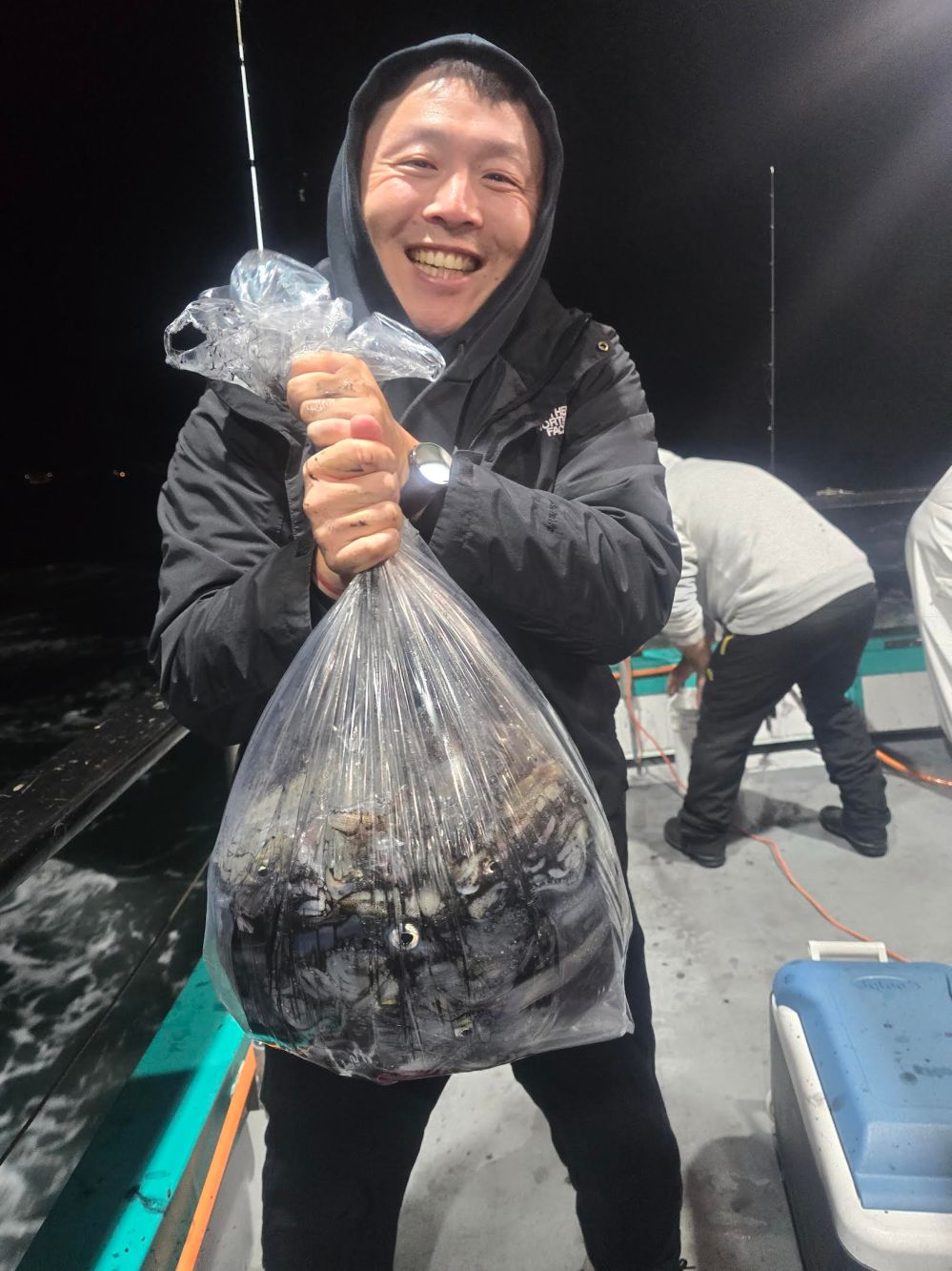 Person smiling on a boat holding a large bag of crabs at night.
