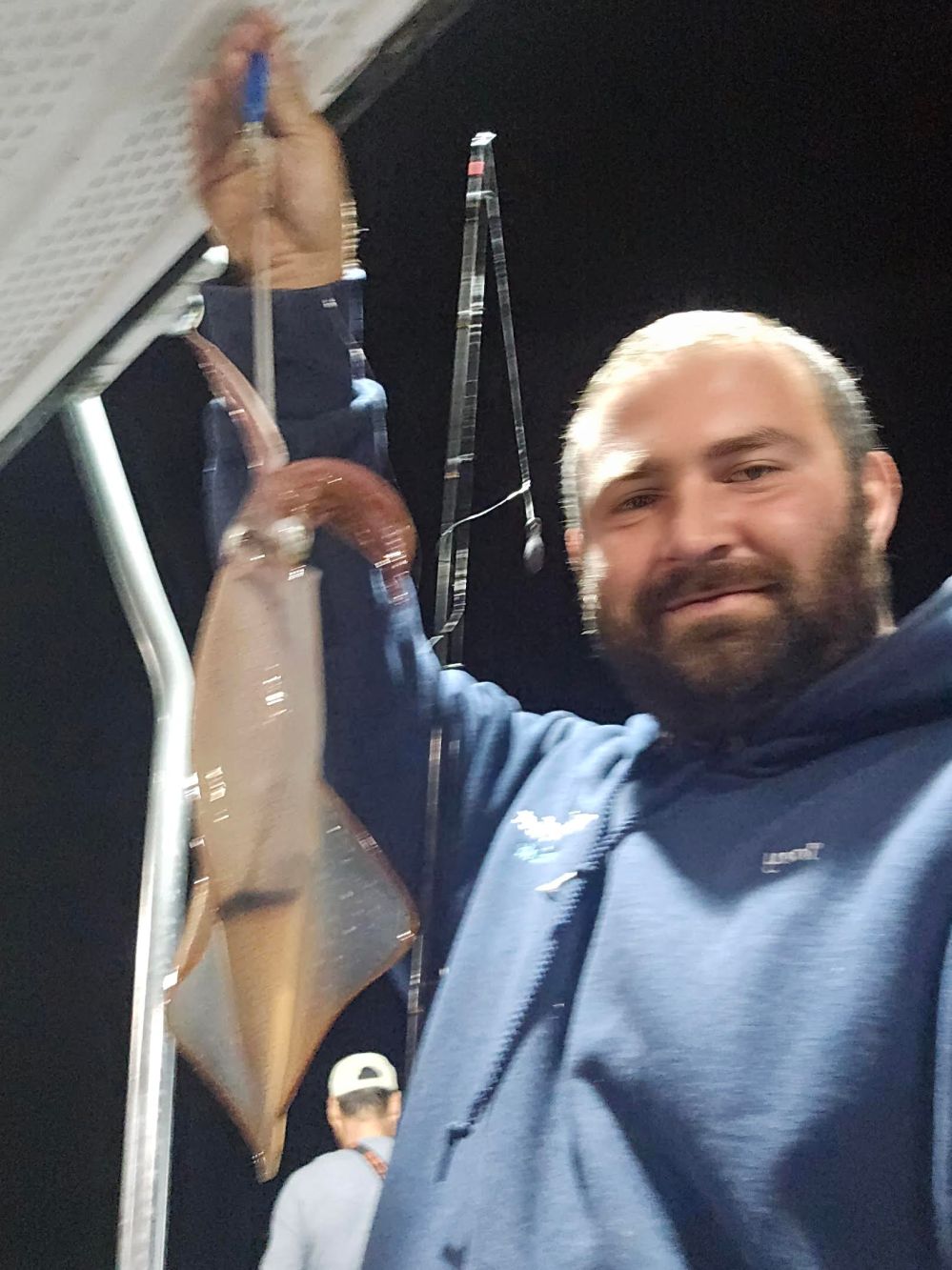 Person holding a squid on a boat at night, with fishing rods in the background.