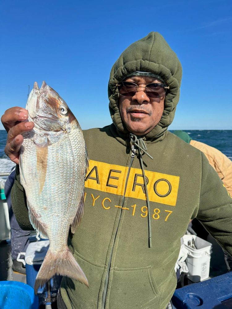 Person in hoodie holding a fish on a boat under a clear blue sky.