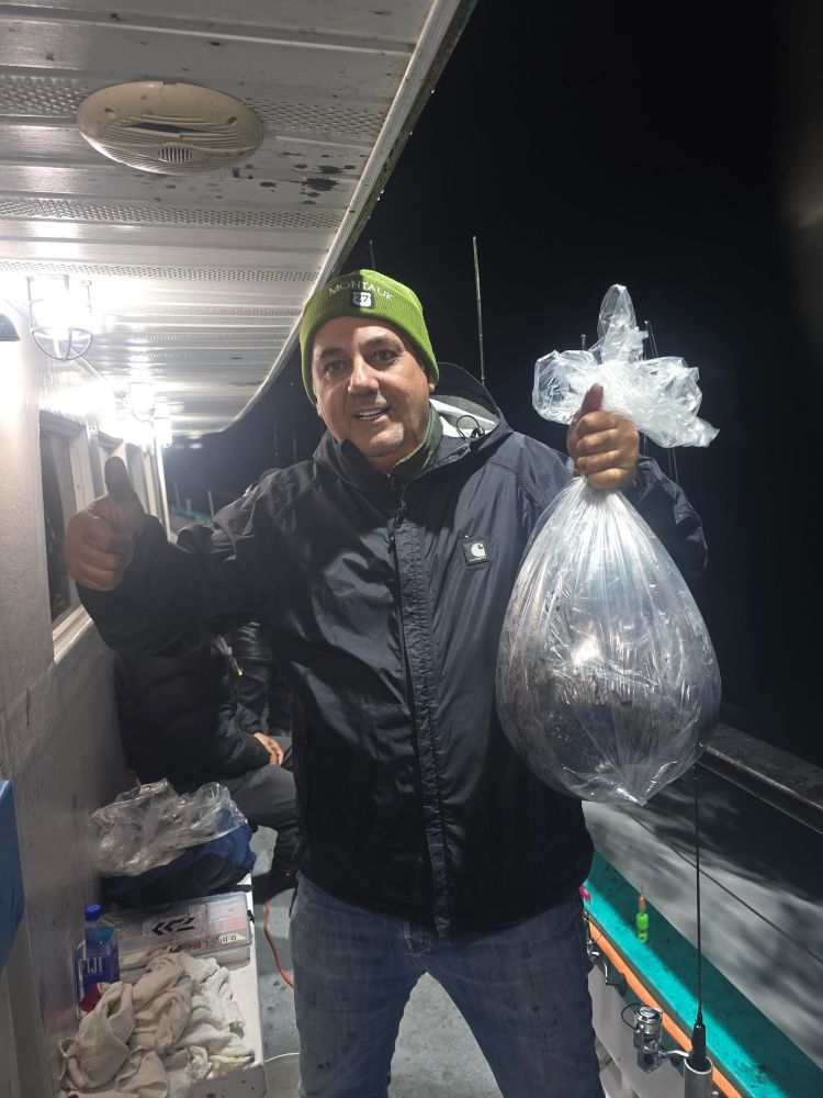 Person on a boat at night holding a bag of fish, giving a thumbs-up.