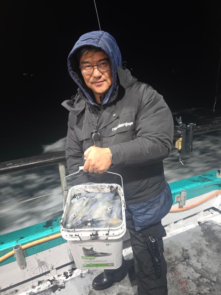 Person on a boat holding a bucket of fish at night, wearing a hooded jacket.