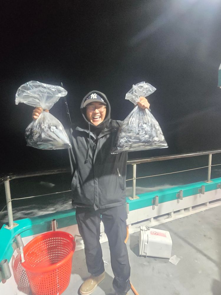 Person on a boat holding two bags of fish at night, smiling and wearing a hat and jacket.