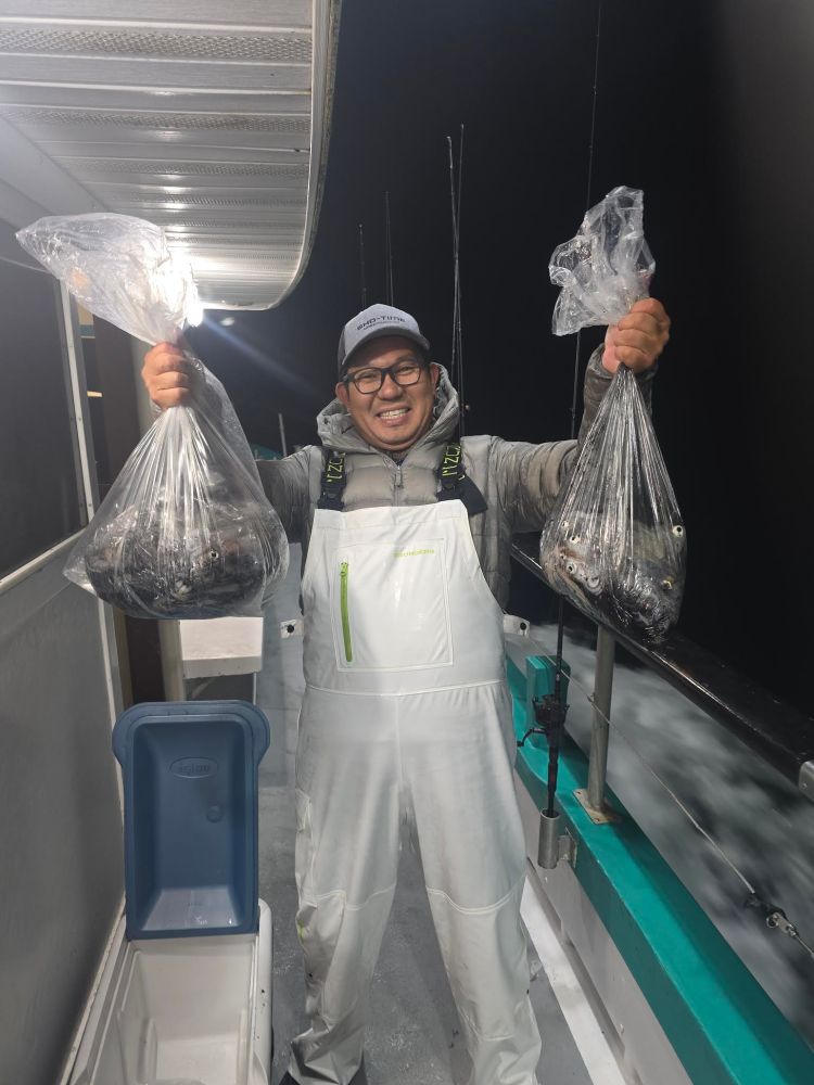 Person in white overalls holding two bags of fish on a boat at night.