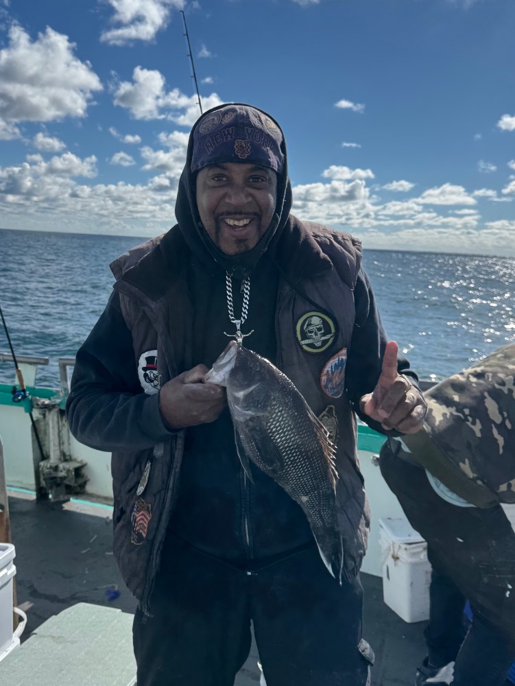A person holding a fish on a boat under a partly cloudy sky.